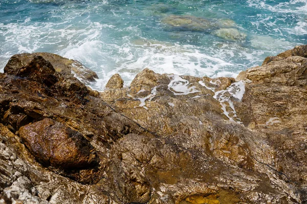 Mavi Akdeniz 'in harika manzarası. Güneşli kayalar, köpüklü dalgalar ve su sıçraması. Dalga kıyıdaki kayalara çarpar.