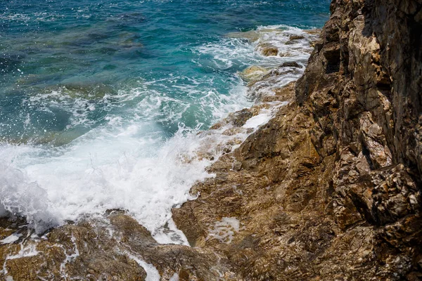 Mavi Akdeniz 'in harika manzarası. Güneşli kayalar, köpüklü dalgalar ve su sıçraması. Dalga kıyıdaki kayalara çarpar.