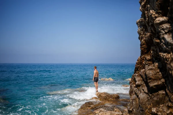 Genç bir adam açık Akdeniz manzaralı kayaların üzerinde duruyor. Sıcak bir yaz günü, güneşli bir günde bir adam deniz esintisine bakar.