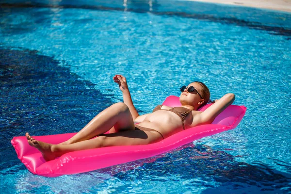 Havuzdaki pembe şişme yatakta mayo giymiş seksi bir kadın yatıyor. Sıcak ve güneşli bir yaz gününde havuz kenarında rahatla. Tatil kavramı
