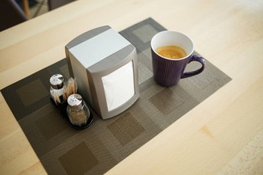 Ahşap masa, servis, tuz ve biber, peçete tutacağı, bir fincan sade kahve.