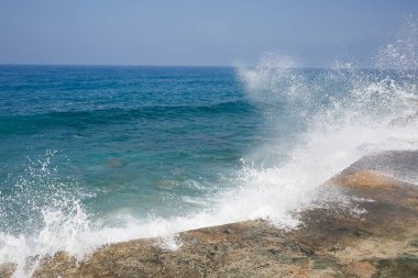 Deniz suyu kayalık kayalara çarpar ve köpükle dalgalar yaratır.