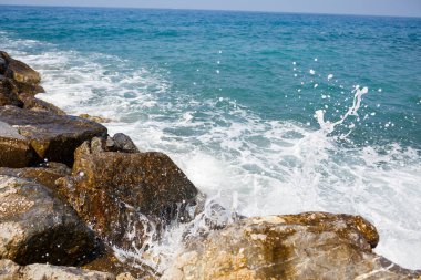 Deniz suyu kayalık kayalara çarpar ve köpükle dalgalar yaratır.