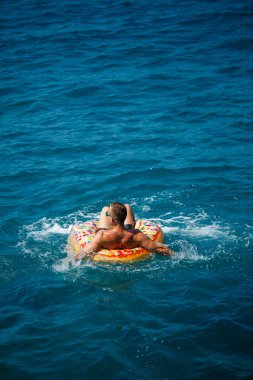 Genç bir adam güneşli bir günde şişme bir yüzükle açık denizde yüzer. Yaz tatili, tatildeki turist.