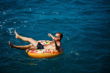 Genç bir adam güneşli bir günde şişme bir yüzükle açık denizde yüzer. Yaz tatili, tatildeki turist.