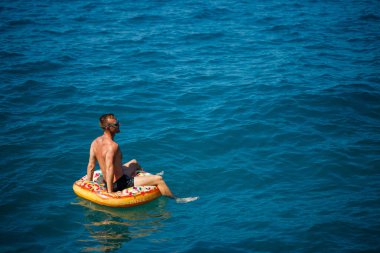Genç bir adam mavi suyla denizde şişirilebilir bir halka üzerinde yüzüyor. Güneşli bir günde güzel bir tatil. Tatil konsepti, üst görünüm.