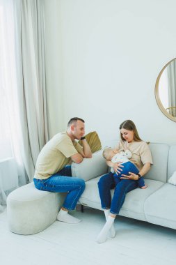 Sıcak ve misafirperver bir oturma odasında, neşeli bir çift değerli yeni doğan bebeklerini kucaklıyor, sevgi, aile ve ebeveynliğin tatmini ile dolu, doyurucu bir anı paylaşıyorlar.