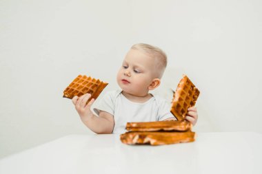 Şirin bir bebek masada oturur ve ilk kez lezzetli tatlar tatmanın saf masumiyetini ve neşesini gösteren renkli bir waffle çeşidini keşfeder.