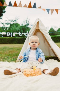 Sevimli bir bebek mutlu bir şekilde dışarıda neşeli bir doğum günü kutlaması yapıyor. Renkli dekorasyonlar ve hoş bir çadırla çevrili. Sevimli anları yakalamak için mükemmel.