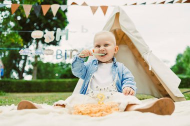 Neşeli bir çocuk, renkli dekorasyonlar ve neşeli atmosferi arttıran bir çadır ile çevrili açık hava partisinde süslü bir doğum günü pastasından hoşlanıyor.