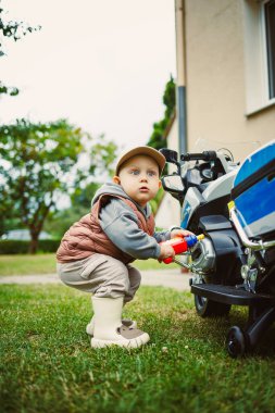 Yeşil bir arka bahçede, rahat kıyafetli neşeli bir çocuk renkli bir oyuncak traktörle neşeyle oynar, çocukluk macerası ve hayal gücünün özünü yakalar.