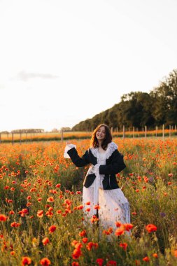 Şık bir kadın günbatımında canlı, çiçek açan çiçeklerin arasında zarif bir şekilde duruyor. Güzellik, huzur ve sanatsal bir karışım olan hem moda hem de doğa ile dolu büyüleyici bir sahne yaratıyor.