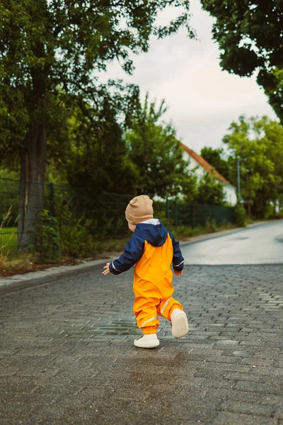 Neşeli bir çocuk, parlak ve canlı yağmur kıyafetleri içinde, neşe içinde boş bir kır yolunda koşmaktan zevk alıyor. Etrafı yemyeşil, karamsar bir gökyüzünün altında.