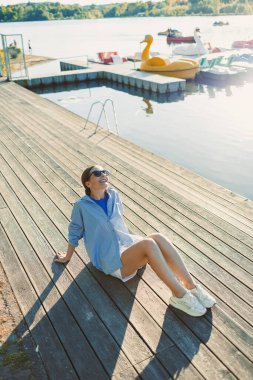 Genç bir insan sakin bir su üzerinde kırsal bir rıhtımda güneşlenirken arkadaşlarıyla renkli kürek çekerken, neşeli yaz eğlencesi ve sükuneti somutlaştırırken,