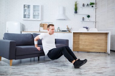 Bir adam şık bir ev ortamında koltuğa triseptik dalış yapar, fitness ve aktif bir yaşam tarzına kendini adadığını gösterir. Ev işleri için mükemmel bir ilham kaynağı..