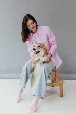 İçeride Corgi Dog 'un yanında oturan mutlu esmer. Keyfi yerinde neşeli bir kız, güzel bir hayvanı okşuyor. İnsan ve evcil hayvan arasındaki arkadaşlık kavramı.