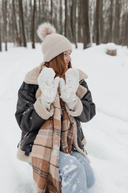 Kış yürüyüşünde boynunda büyük, sıcak bir eşarp olan kürklü güzel bir kadın. Kadın kışın karda gülümser ve sevinir. Kız kışın karlı bir parkta yürüyor..