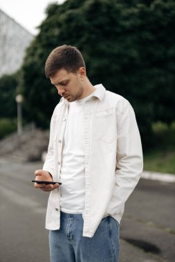 Şık, genç bir adam akıllı telefonuyla derinden özümsenmiş modern şehir hayatının ve dijital etkileşimin özünü yakalıyor, hepsi sakin ve güzel bir arka plana karşı kurulmuş.