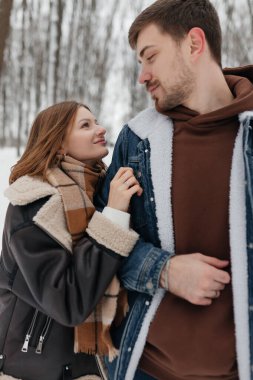 Sevimli bir çift, kar kaplı ağaçlarla çevrili büyülü kış harikalar diyarında keyifli bir anın tadını çıkarır. Sıcak giysiler içinde sıcaklık ve neşe saçar.