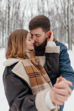 Resimli bir kar ormanında, sevgi dolu bir çift tutkulu bir öpücüğü paylaşır, eşleşen kış kıyafetleri doğada bulunan büyüleyici aşk büyüsünü güzel bir şekilde sergiler.