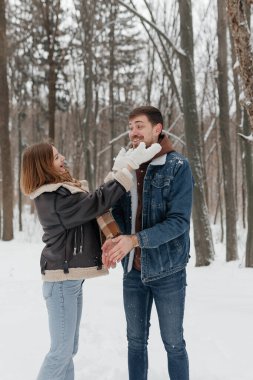 Neşeli bir çift, karlı bir ormanda, uzun ağaçlarla çevrili güzel ve eğlenceli bir anı paylaşır. Aşkın sıcaklığını ve kışın soğuğunun sağladığı eğlenceyi somutlaştırır.