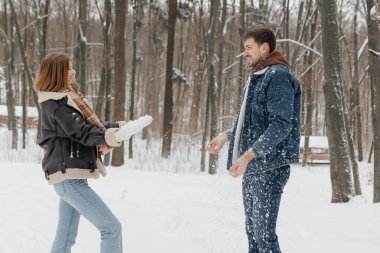 Neşeli bir çift, neşeli bir şekilde karların üzerinde oynuyor. Etrafı, sakin bir kış manzarasında, uzun ve yeşil ağaçlarla çevrili. Eğlencenin ve birlikteliğin güzelliğini sergiliyorlar.