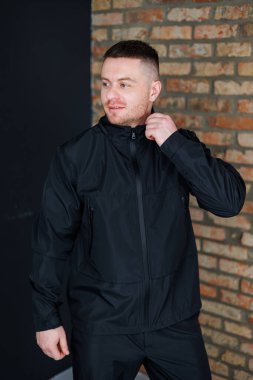 Şık ve modaya uygun bir genç adam, gösterişli siyah bir ceket giyerken, eşsiz şehir stilini endüstriyel bir ortamda dokulu tuğla bir arka planda sergiliyor.