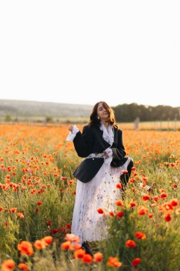 Bir kadın, altın saatinde canlı bir haşhaş tarlasında zarif bir poz verir doğal güzelliği, büyüleyici ve sakin bir görsel deneyim için yüksek modayla harmanlar.