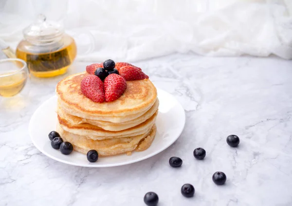 Stack di frittelle con guarnizione, fragola e mirtillo.Posizionato in un piatto bianco su un tavolo di marmo e copiare spazio.Mangiare con il tè nel bicchiere . — Foto Stock