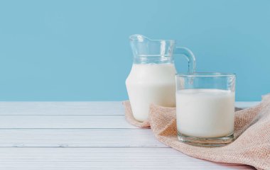 Bardaktaki doğal taze süt ve sürahi, mavi arka plandaki ahşap bir masanın üzerindeki bir peçeteye konur. Sağlıklı beslenmek.