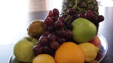 Meyve tabağı. Ananas, elma, kırmızı üzüm, limon, portakal. Kamera etrafında hareket eder.