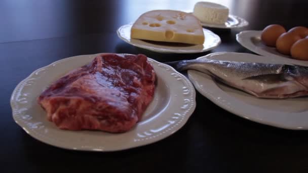 高蛋白食物。生肉和鱼，奶酪，鸡蛋在单独的盘子。相机在右边移动 — 图库视频影像