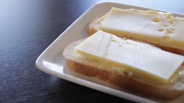 Bir tabakta tereyağı ve peynir ile 2 beyaz ekmek sandviç. kamera bunun etrafında sağa doğru hareket eder. Close