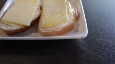 Bir tabakta tereyağı ve peynir ile 2 beyaz ekmek sandviç. kamera bunun etrafından sola doğru hareket eder. Close