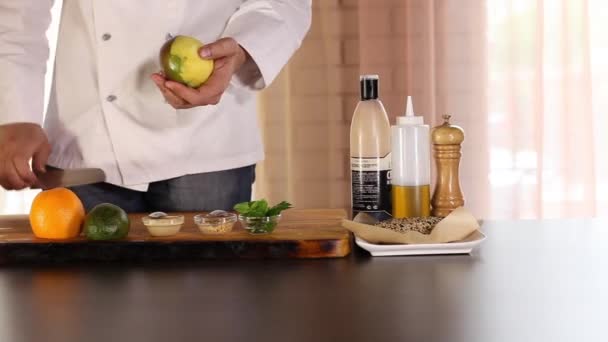 O chef está limpando a manga com uma faca. Há uma laranja na mesa, um abacate, folhas de salada. . — Vídeo de Stock