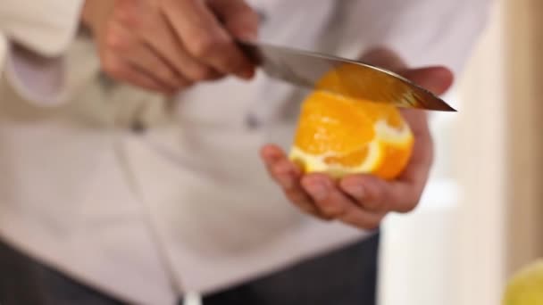 As mãos dos chefs cortam uma laranja com uma faca.close-up — Vídeo de Stock