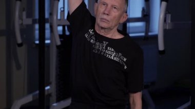 Yaş bir adam spor salonunda ortak jimnastik yapar. Kolu dikey olarak yukarı doğru yukarı doğru yükseltmek ve gövdeyi yana doğru eğmek. Close