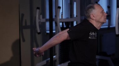 Çağın bir adam spor salonunda arka için ortak jimnastik yapar. Arkadaki kolların düzeşle düzeltilmesi. Close