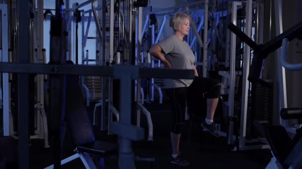 En äldre kvinna gör knä-hissar stående upp. tränar gemensam gymnastik. Kopiera mellanslag. sidovy — Stockvideo