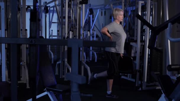 Oudere vrouw voert een staande flexon van het been. gezamenlijke gymnastiek. Kopieer ruimte. zijaanzicht — Stockvideo