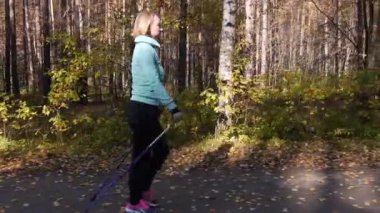 Bir sonbahar parkında Nordic Walking'i uygulayan bir kadın. Yakındaki bir arabadan hareket halindeçerçeve. Yan görünüm