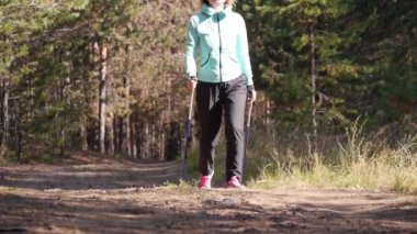 Bir sonbahar ormanında Nordic Walking pratik kadın, o kumlu yolda kameraya gidiyor. Ön görünüm