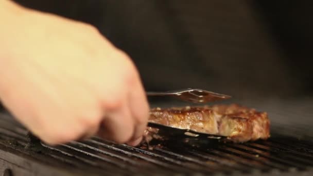 La mano degli chef gira la bistecca di manzo sulla griglia con le pinze. — Video Stock