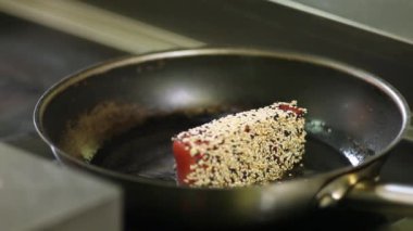 Sıcak bir tavada susam bir ton balığı biftek bunded kavurma işlemi. Aşçı bifteği ters çeviriyor.