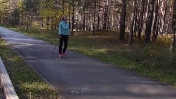 Donna che pratica il Nordic Walking in un parco autunnale. Cornice in movimento da una macchina vicina. Vista frontale diagonale — Video Stock