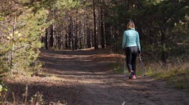 Bir sonbahar ormanında Nordic Walking pratik kadın, o kumlu yolda kamera dan uzaklaşırken. Geri görünüm. Geniş açı çekim