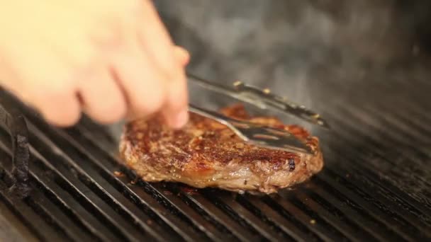 O chef vira o bife de carne fumegante na grelha.close-up — Vídeo de Stock