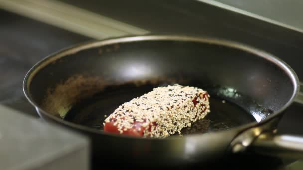 O chef transforma um pedaço de filé de atum, amontoado em gergelim, em uma panela quente durante o ato de fritar — Vídeo de Stock