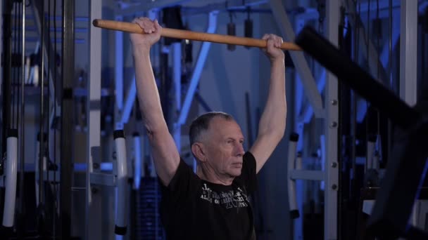 Um homem idoso faz um exercício isométrico com uma vara, segurando-o sobre sua visão head.side. — Vídeo de Stock