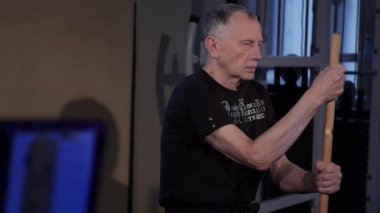 stick.an yaşlı bir adam ile isometrik egzersiz bir oturma pozisyonunda önünde dikey bir sopa tutar. Space.glide cam görüntüleri kopyalayın.yan görünüm